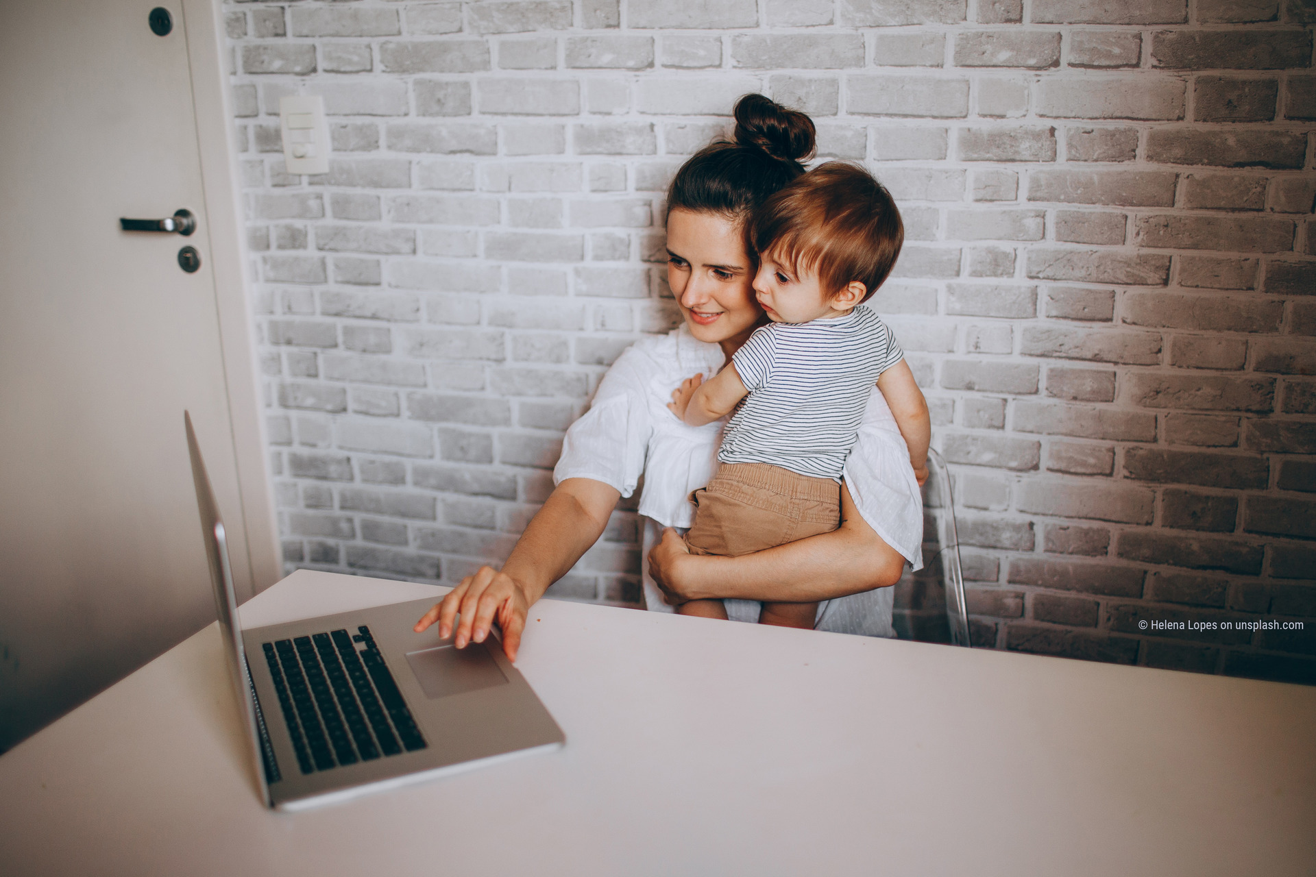 Frau mit Kleinkind im Arm arbeitet mit der anderen Hand am Laptop